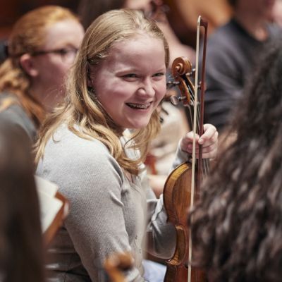 Junior Guildhall student laughing on stage holding her violin
